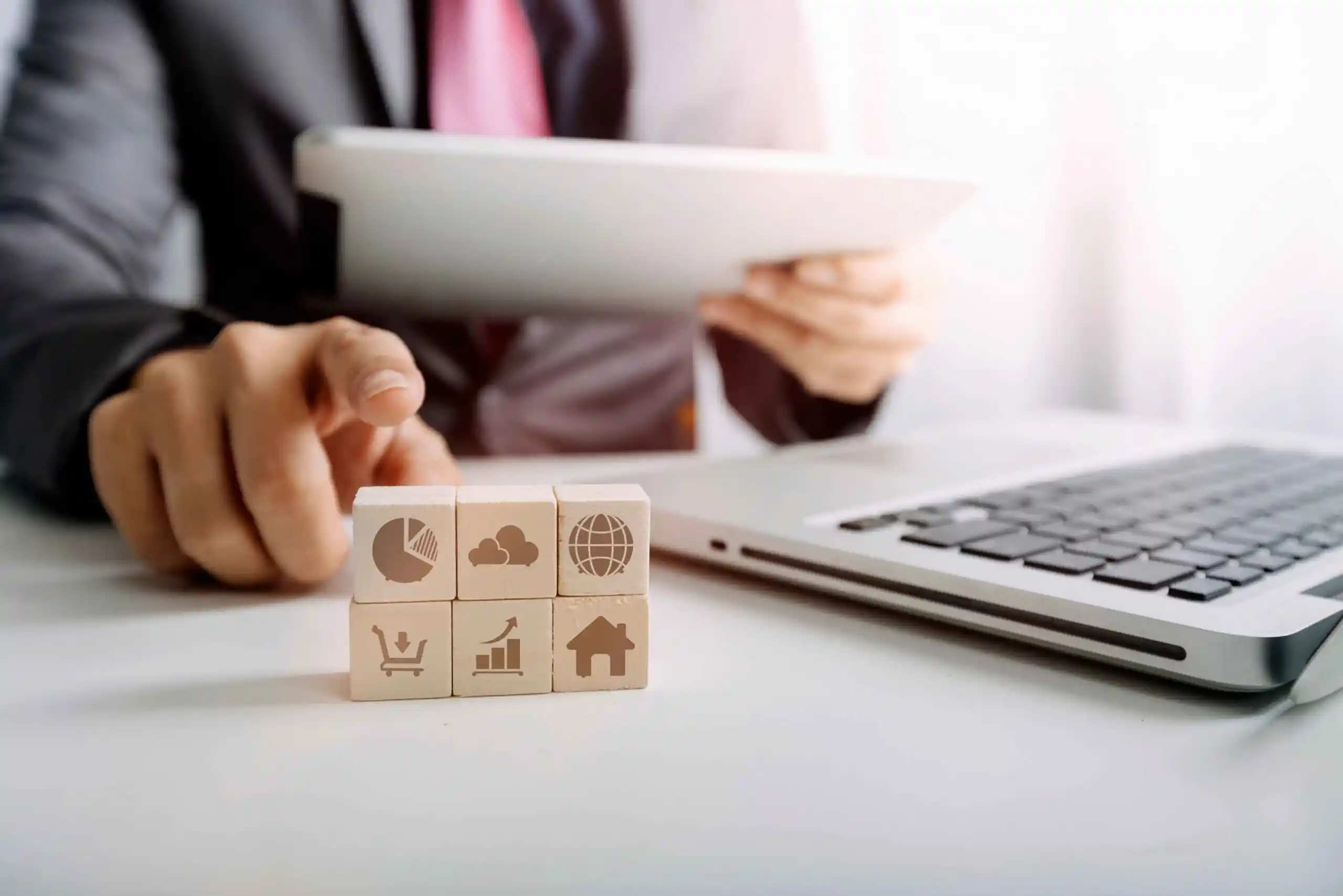 Person arranging wooden blocks with business icons beside a laptop