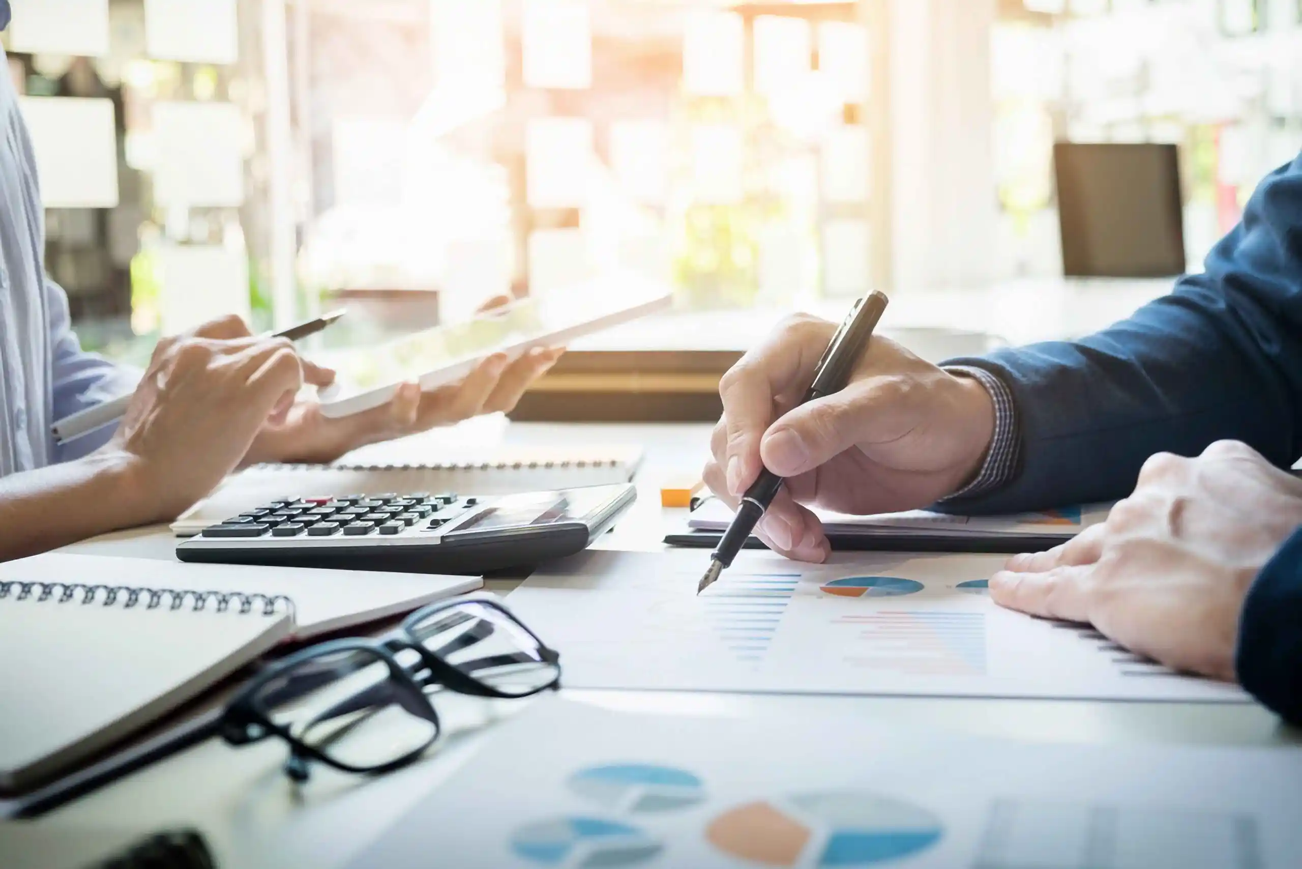 Two people reviewing financial charts with a calculator at a desk